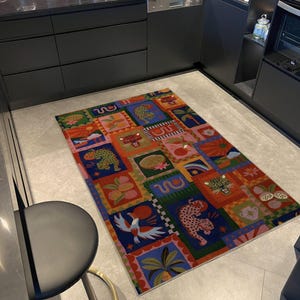 May include: A colorful rectangular rug with a patchwork design featuring various animal and plant illustrations. The rug's squares display leopards, birds, and fruits in vibrant hues of red, blue, green, and orange. The rug is placed on a light gray tiled floor.