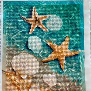 May include: Diamond painting kit depicting a detailed underwater scene. The image shows two starfish, seashells, and a sandy seabed, all rendered in small, colourful, sparkling beads. The design size is 36 x 27 cm.