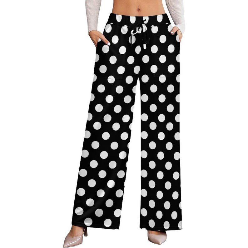Woman wearing high-waisted, wide-leg pants with a bold black and white polka dot pattern, hands in pockets; paired with a white top and beige heels.