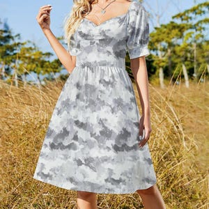 May include: A white and gray tie-dye print dress with short, puffed sleeves and a sweetheart neckline. The dress has a fitted bodice and a flared skirt, creating a feminine silhouette. The dress is knee-length and suitable for casual wear.
