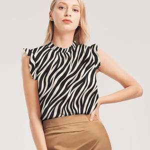 Pode incluir: Uma blusa sem mangas com estampa de zebra em preto e branco. A parte de cima tem gola alta e mangas curtas com babados. A modelo está usando uma saia marrom.