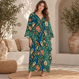 May include: A floor-length kaftan dress featuring a deep teal background with a repeating pattern of blue and green peacocks, orange flowers, and green foliage. The garment has a V-neckline and wide, loose-fitting three-quarter length sleeves.