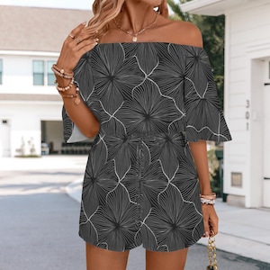 May include: Black and white floral print romper with an off-the-shoulder neckline and short sleeves. The romper features a tie waist and a playful, summery design. The fabric has a delicate, flowing quality, perfect for warm weather.