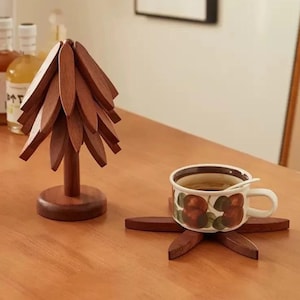 Puede incluir: Una escultura de madera en forma de árbol y un posavasos a juego con una taza de té sobre una mesa de madera. La taza tiene un diseño floral. La escultura está hecha de muchas piezas pequeñas de madera. El posavasos está hecho de seis piezas de madera.