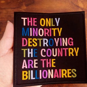 May include: Black square patch with embroidered text in various colors: "THE ONLY MINORITY DESTROYING THE COUNTRY ARE THE BILLIONAIRES."