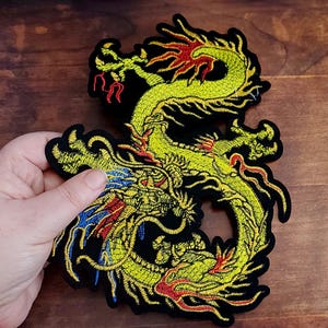 Peut inclure: Écusson brodé d'un dragon jaune, rouge et bleu sur fond noir. Le motif du dragon présente des détails complexes et un aspect stylisé. Le patch est destiné aux vêtements ou accessoires.