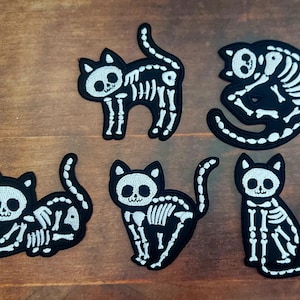 May include: Five black cat skeleton patches with white embroidered details. The patches feature various cat poses, including standing, sitting, and curled up. Ideal for Halloween or spooky-themed crafts.