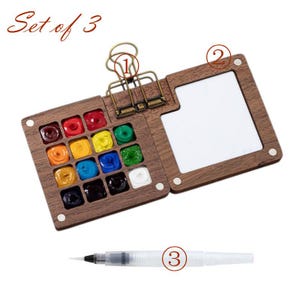May include: A wooden watercolor paint set with a hinged lid, featuring a palette of vibrant colors and a built-in mixing area. Includes a water brush and is labeled "Set of 3". The set is designed for artists and hobbyists.