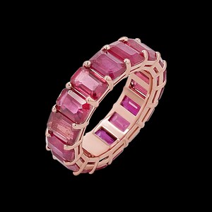 May include: An eternity band ring crafted from rose gold, featuring a continuous row of emerald-cut, deep pinkish-red gemstones set in individual prongs that encircle the entire circumference of the band, showcasing a uniform and symmetrical design.