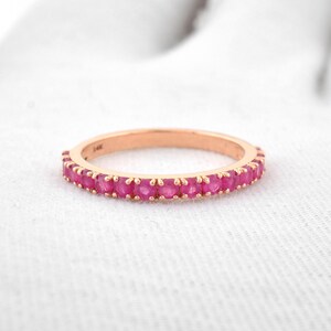 Puede incluir: Anillo de oro rosa con una banda de gemas rosas vibrantes. El anillo se encuentra sobre una superficie blanca, mostrando el contraste entre el metal y las gemas. Una joya.