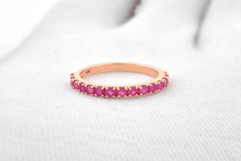 Puede incluir: Anillo de oro rosa con una banda de gemas rosas vibrantes. El anillo se encuentra sobre una superficie blanca, mostrando el contraste entre el metal y las gemas. Una joya.