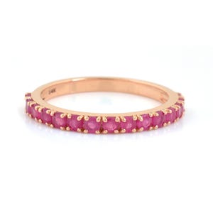 Puede incluir: Un anillo de oro rosa con una banda de peque&ntilde;as gemas redondas de color rosa brillante. El anillo est&aacute; sobre un fondo blanco, resaltando el color y el dise&ntilde;o. Una delicada pieza de joyer&iacute;a.