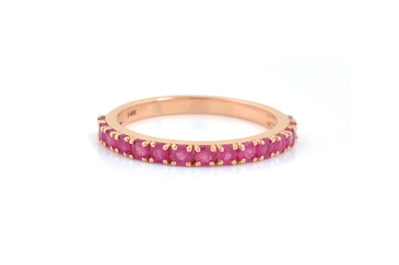 Puede incluir: Un anillo de oro rosa con una banda de peque&ntilde;as gemas redondas de color rosa brillante. El anillo est&aacute; sobre un fondo blanco, resaltando el color y el dise&ntilde;o. Una delicada pieza de joyer&iacute;a.