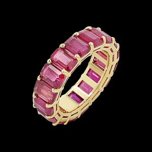 May include: An eternity band ring crafted from yellow gold, featuring a continuous row of rectangular emerald-cut red rubies set in individual prongs that encircle the entire circumference of the band, showcasing a vibrant and uniform gemstone design.