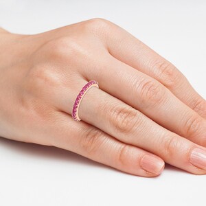 Puede incluir: Un anillo de oro rosa con una banda de peque&ntilde;as y vibrantes piedras preciosas rosas. El anillo se lleva en el dedo de una persona, mostrando el delicado dise&ntilde;o y color. El anillo es una joya.