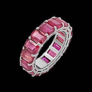 May include: A silver-toned eternity band ring featuring a continuous row of rectangular, emerald-cut red gemstones set in a prong setting. The ring has a polished metallic finish and showcases a series of vibrant, deep pinkish-red stones.
