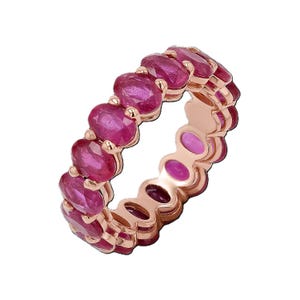 Può includere: Un anello a fascia eternity con una fila continua di rubini rosso rosato intenso a taglio ovale, incastonati in una banda in oro rosa lucido. Le pietre sono fissate con griffe, creando un design circolare che esalta il colore vivido delle gemme.
