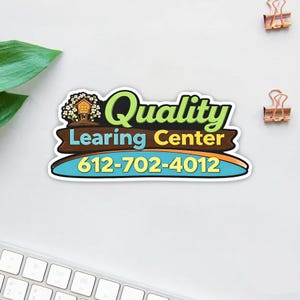 May include: A colorful sticker with the words "Quality Learning Center" and a phone number. The sticker features a treehouse graphic and a blue, yellow, and brown design. The phone number is 612-702-4012.