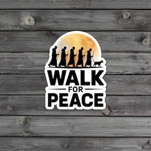 Könnte beinhalten: Ein weißer Aufkleber mit dem Text "WALK FOR PEACE" in Schwarz. Über dem Text befindet sich eine Silhouette von Menschen, die mit einem Hund gehen, vor einem gelben Mond.