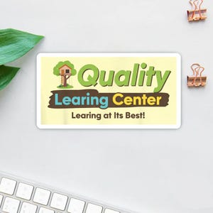 Könnte beinhalten: Ein rechteckiger Aufkleber mit den Worten "Quality Learning Center" in Grün und Blau, mit einer Baumhaus-Grafik. Der Text "Learning at Its Best!" steht darunter. Der Aufkleber liegt auf einer weißen Oberfläche mit zwei goldenen Büroklammern.