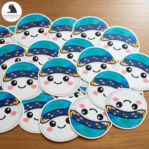 Puede incluir: Una colección de pegatinas redondas con un personaje de dibujos animados sonriente con un sombrero azul y turquesa adornado con estrellas amarillas. El personaje tiene mejillas rosadas y una expresión feliz. Las pegatinas son blancas con un borde azul oscuro.