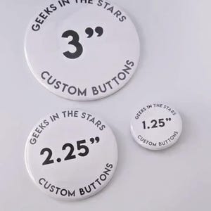 May include: Three white custom buttons with black text. The largest button is 3 inches in diameter, the middle one is 2.25 inches, and the smallest is 1.25 inches. Each button has the text "GEEKS IN THE STARS" and "CUSTOM BUTTONS".