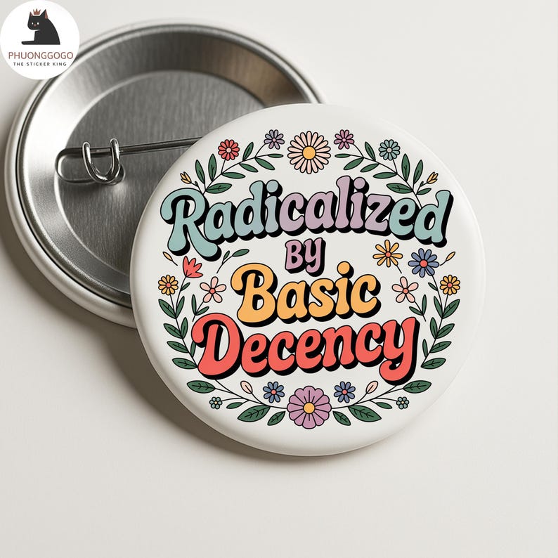 May include: A white button pin with the text "Radicalized by Basic Decency" in a retro font, surrounded by colorful flowers and leaves. The pin has a metal back and a safety pin closure.