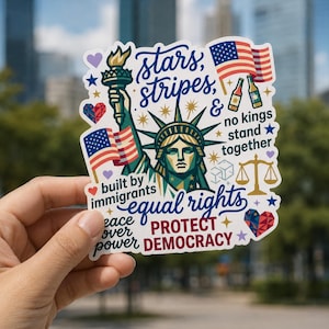 May include: A die-cut sticker featuring the Statue of Liberty in green, surrounded by American flags, a scale of justice, and hearts. Text reads: stars, stripes, & no kings stand together, built by immigrants, equal rights, peace over power, PROTECT DEMOCRACY.