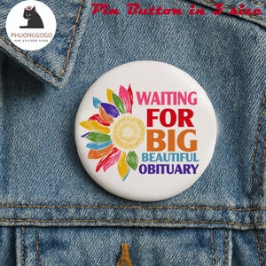 以下が含まれることがあります： カラフルなヒマワリのデザインと「WAITING FOR BIG BEAUTIFUL OBITUARY」という言葉がピンク、赤、オレンジ、青で書かれた白いピンボタン。ピンはデニムジャケットに付いています。