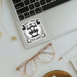 Op de afbeelding: Een zwart-witte sticker met een ridder die een halter optilt. De sticker heeft de tekst "DOST THOU EVEN HOIST?" in een decoratief lettertype. De sticker zit op een laptop.