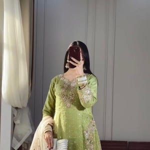 May include: A light green embroidered salwar kameez set. The long-sleeved tunic and matching trousers are decorated with intricate gold and white floral embroidery. A cream-coloured dupatta with gold trim and a white clutch complete the ensemble.