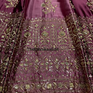 May include: Close-up of a maroon fabric with intricate gold embroidery and sequin embellishments. The design features floral and geometric patterns. The text "TheEthnikaaEdit" is visible on the fabric.