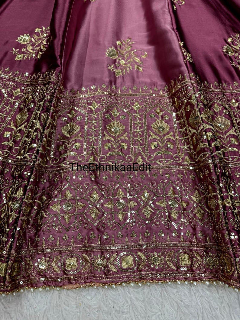 May include: Close-up of a maroon fabric with intricate gold embroidery and sequin embellishments. The design features floral and geometric patterns. The text "TheEthnikaaEdit" is visible on the fabric.