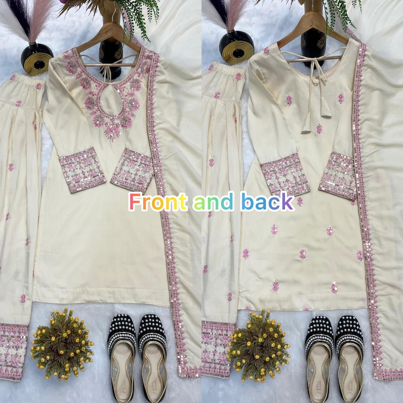 May include: Cream-colored embroidered salwar kameez set with pink accents. The set includes a long-sleeved tunic, matching pants, and a scarf. The tunic features intricate embroidery around the neckline and cuffs. The text "Front and back" is visible.