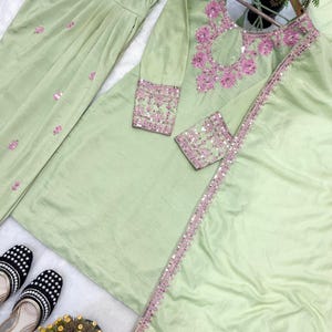 May include: A light green, long-sleeved tunic and matching pants set with pink embroidery and sequin accents. The tunic features a keyhole neckline and decorative trim. Black and white patterned shoes are visible.