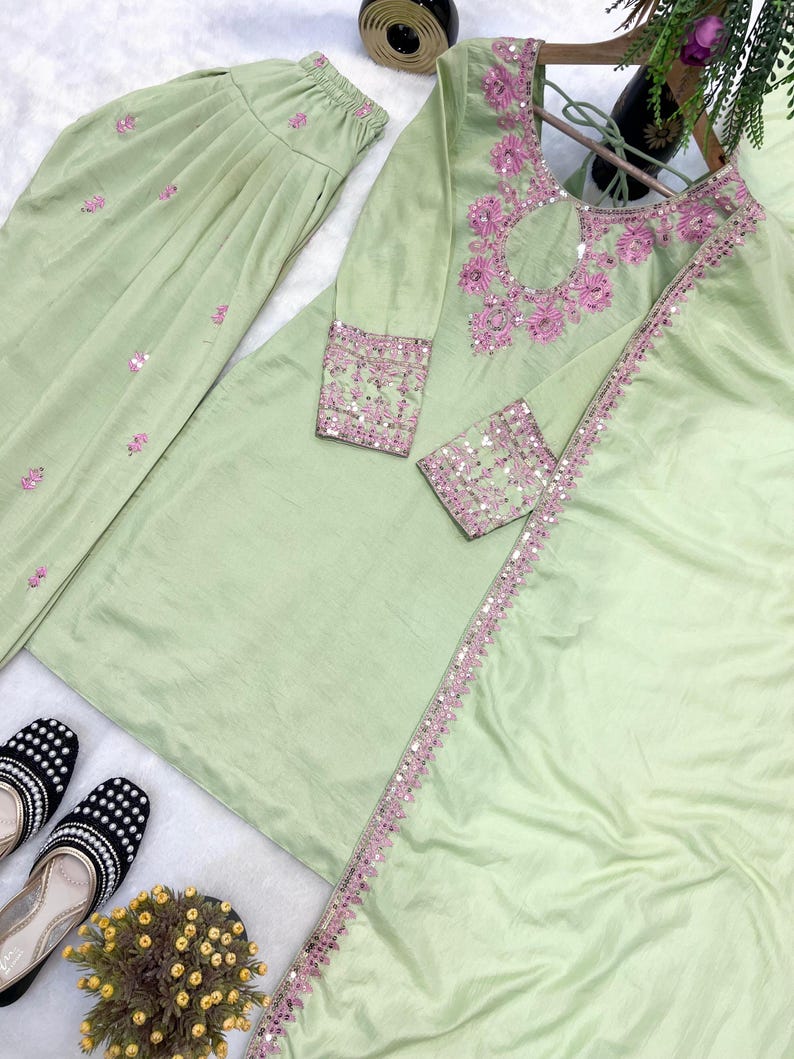 May include: A light green, long-sleeved tunic and matching pants set with pink embroidery and sequin accents. The tunic features a keyhole neckline and decorative trim. Black and white patterned shoes are visible.