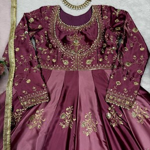 May include: A burgundy and mauve-colored formal dress with long sleeves. The dress features intricate gold embroidery on the bodice and sleeves, with a flowing skirt. A gold necklace with a pink flower and the text "TheEthnikaaEdit" are also visible.