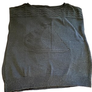 May include: A black sleeveless knit sweater featuring a textured wave pattern across the upper chest and shoulders. The center of the garment displays a prominent tonal knit design of a sailboat. The sweater has a ribbed hem at the bottom.