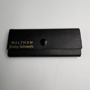 May include: A rectangular black case with a textured surface and a single snap button closure. The text WALTHAM Drawing Instruments is printed in gold lettering on the front flap of the case, which is designed to hold various drafting tools.