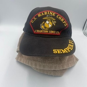 May include: Black baseball cap with the U.S. Marine Corps emblem, featuring a red and gold patch with the words "U.S. Marine Corps" and "A Tradition Since 1775." The cap also has the words "Semper Fi" embroidered in gold.