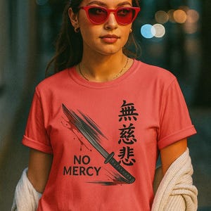 May include: A coral-colored t-shirt featuring a black katana design with the words "NO MERCY" and Japanese characters. The shirt has short sleeves.