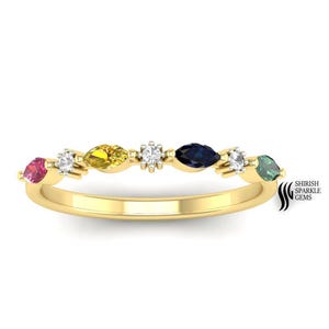 May include: A gold band ring featuring a series of colorful gemstones. The ring showcases a sequence of marquise-cut gems in various colors, including pink, yellow, blue, and green, interspersed with smaller white stones. The ring is set against a white background.