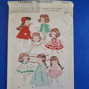 May include: Vintage Butterick printed patterns envelope featuring illustrations of dolls in various outfits. The text reads "LENGTH OF DOLL 8 INCHES IN THIS SIZE ONLY". The envelope is off-white with a blue background.