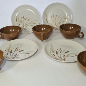 May include: A vintage dinnerware set featuring cream-colored plates and bowls with a brown interior. The plates and cups have a wheat stalk design in gold and brown. The set includes plates, cups, and bowls.