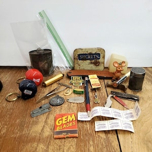 May include: A collection of vintage items, including keychains, a small tin of Sucrets lozenges, a Gem Blades box, a pen, and a small mouse figurine. The items are arranged on a wooden surface.