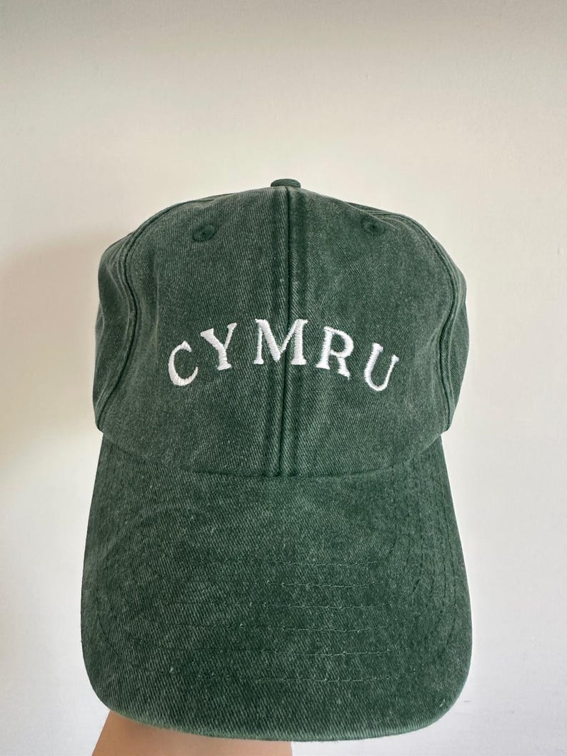 以下が含まれることがあります： 前面に白で「CYMRU」の文字が刺繍された濃い緑色の野球帽。 つばがカーブしており、上部が丸くなっています。 帽子は柔らかく、質感のある生地で作られています。