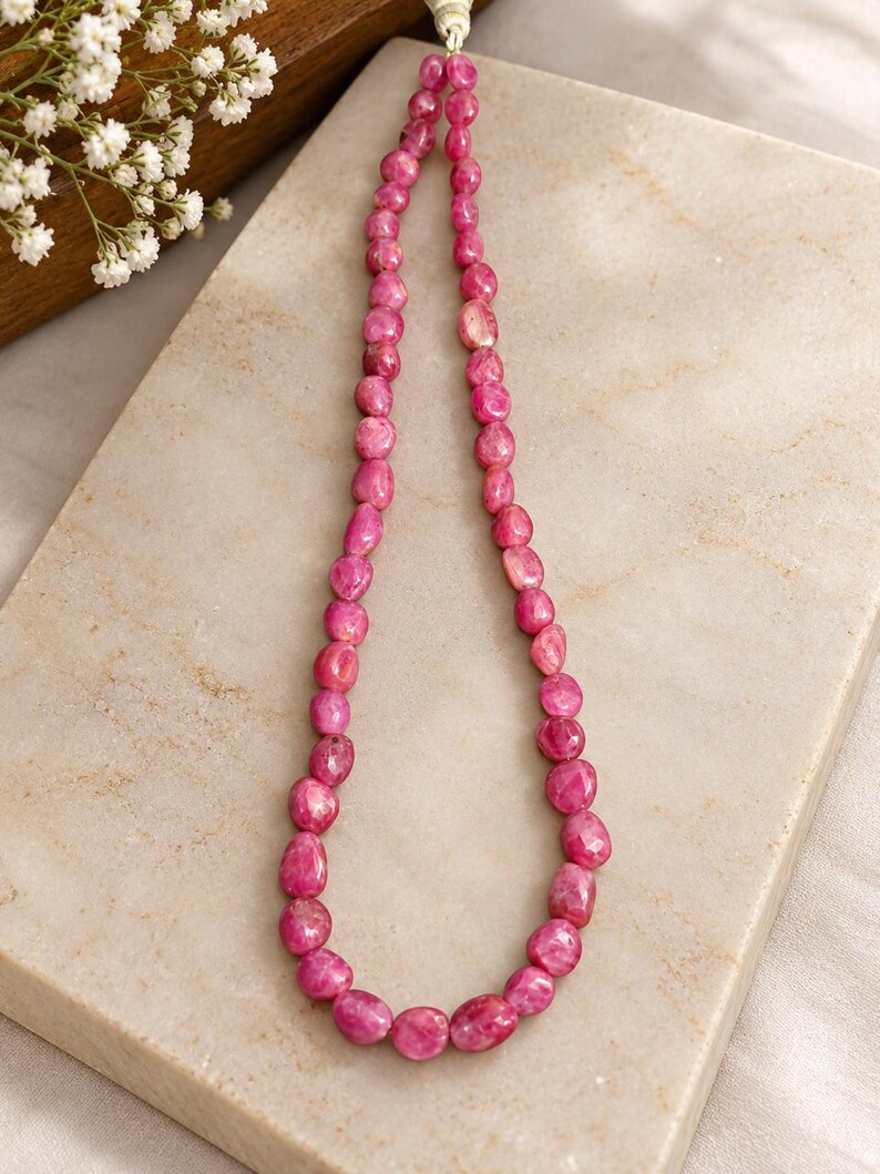 May include: A single strand necklace composed of numerous small, faceted, irregular pink gemstone beads. The beads are strung on a light-coloured cord, creating a continuous loop of vibrant, polished stones with varying shapes and sizes.