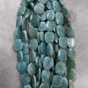 May include: Strand of Amazonite gemstone beads. The beads are a mix of light blue and green hues, with a polished, irregular shape. The beads are strung together, creating a necklace or bracelet.