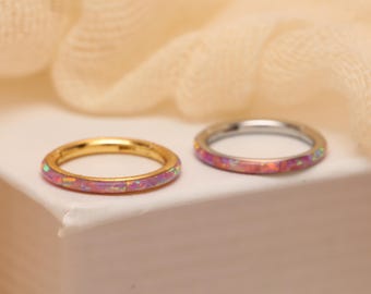Puede incluir: Dos anillos circulares delgados con una incrustación lisa de material rosa similar al ópalo. Un anillo tiene un acabado de metal dorado pulido, mientras que el otro tiene un acabado de metal plateado pulido. Ambos tienen un diseño sencillo.
