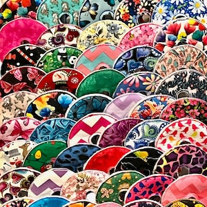 May include: A collection of colorful, patterned round objects, possibly coasters or decorative items. The designs include floral, butterfly, and geometric patterns in a variety of colors like pink, blue, green, and red. The items are arranged in a layered, overlapping fashion.